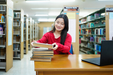 Female student with stack of books sitting at table in library