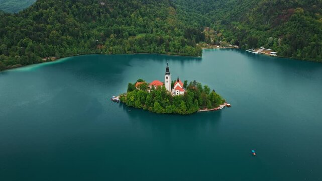 Aerial view of Church of the Assumption of Mary in the center of the lake Bled. Flying around small island on Bled Lake in Slovenia