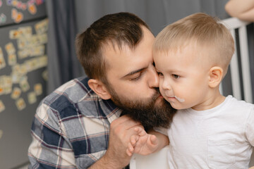 Affectionate caucasian male adult kissing blonde child in cozy home setting, Lifestyle moment of...