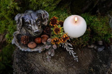 vintage cast-iron figurine in the form of a dog's head, flowers, cones, acorns, burning candle close up on tree stump. witchcraft, magic ritual for wellbeing, rich harvest, successful hunting