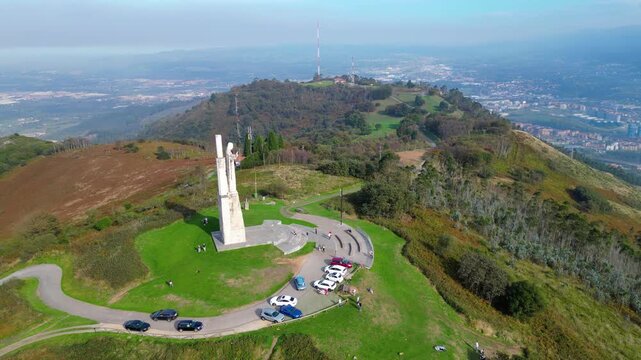 Panoramic aerial view of Oviedo city and the surrounding Asturian landscape, featuring the iconic Cristo del Monte Naranco statue under a cloudy autumn sky.