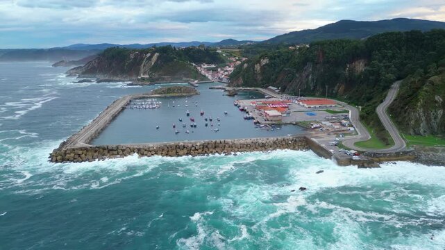 Aerial view of Cudillero, a charming Asturian fishing village, nestled between rugged cliffs and the turbulent Cantabrian Sea at dusk.
