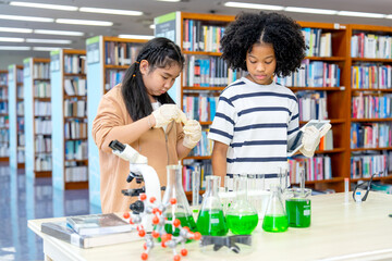 Close up two girls enjoy to study with science experiment by mix green solution with test tube in area of public library.