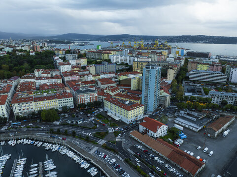 Aerial view of red roofs meet the Adriatic's edge, while the Molo Audace pier stretches into the sea under a brooding sky, Trieste, Friuli-Venezia Giulia, Italy.