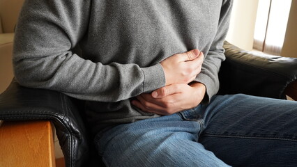 A man sitting in an armchair clutches his belly due to stomach ache