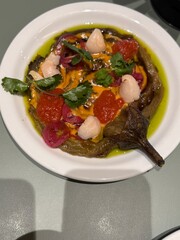 Eggplant dish with colorful toppings and herbs on white plate, viewed from above