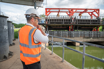 an engineer in safety vest inspects water gate structure, recording data on a sunny day