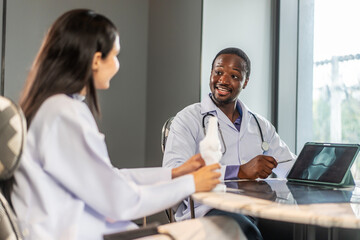 In a hospital, male and female medics discuss human skeleton anatomy. They use a tablet and a model...