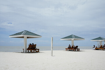 relaxing beach scene with umbrella shaded loungers over white sand and calm sea, blue sky