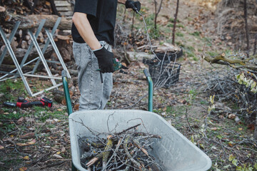 A young woman working in the garden using hand pruning shears to cut dry branches.