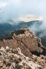 Majestic rocky cliffs rise through mist and clouds in the Puig Campana region, Spain, perfect for nature, adventure, hiking, and travel inspiration in scenic mountain environments.