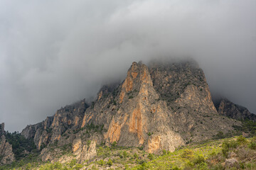 Moody clouds envelop the rugged peaks of Puig Campana in Spain, creating a dramatic and atmospheric mountain landscape ideal for nature, travel, and adventure themes.