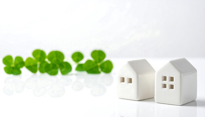 清潔な白背景にクローバーと一戸建て模型が並ぶ不動産の穏やかで希望的な風景