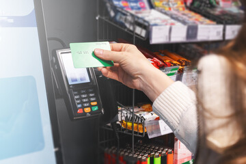 Payment by credit card at the self-service terminal with a touch screen in the store. A woman puts a credit card to the terminal close-up