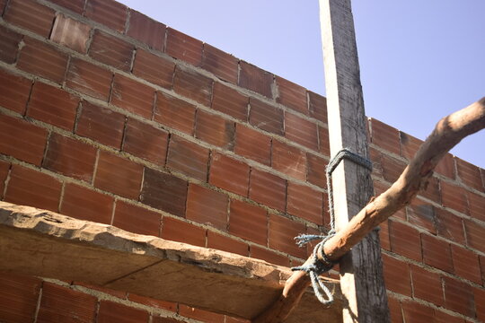 Suportes de madeira improvisados para o levantamento de parede de alvenaria com tijolos vermelhos furados em casa brasileira