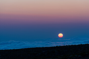 Soleil se couchant dans des couleurs pastel au dessus d'une mer de nuages sur l'île de la Réunion, France