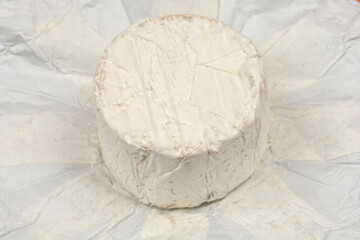 A whole round of creamy Camembert or Brie cheese with a white bloomy rind sits unwrapped on its paper