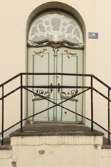 Charming old wooden door painted green and white, framed by red bricks. A lavender wreath and a pot of blooming purple flowers create a welcoming and picturesque rustic entrance