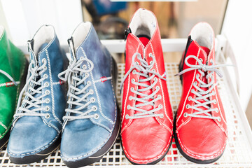 A vibrant collection of handmade leather boots in bold green, blue, and red hues displayed on a shelf. Artistic stitching and contrasting laces emphasize fashion, creativity, and individuality
