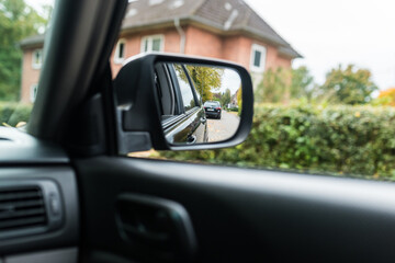 driving a car. Car side mirror showing a suburban road lined with trees and hedges on an autumn day. A realistic view from inside the vehicle illustrating transportation, safety