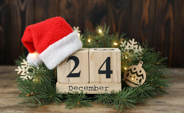 Rustic Wooden Calendar Blocks Displaying December 24th with a Santa Hat and Festive Christmas Wreath Decorations on a Table