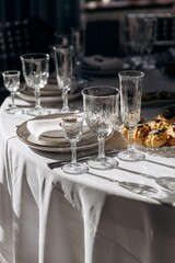 Close-up of glassware and place setting on a white table, sharply illuminated by a patch of bright sunlight and deep shadows
