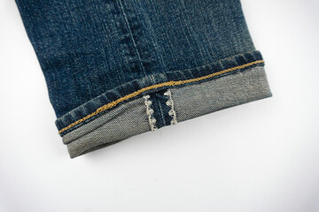 Detailed view of blue denim jeans cuff showing stitching, fold, and texture on white background