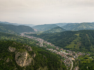 Obraz premium Aerial drone view of mountain town in green valley with forested hills