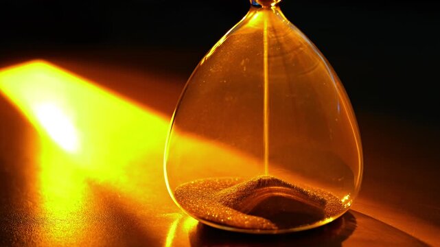 A video frame of an hourglass where golden sand flows, powerfully symbolizing the irreversible passing of time under dramatic, warm light.