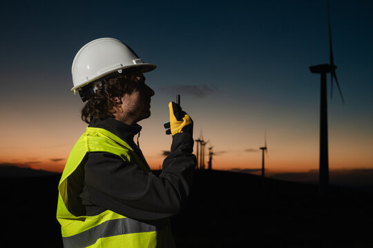 Engineer using radio communication at wind farm during sunset, Spain