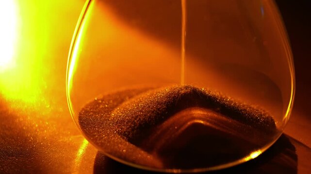 A video frame of an hourglass where golden sand flows, powerfully symbolizing the irreversible passing of time under dramatic, warm light.