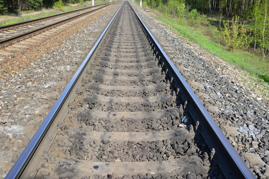 Parallel railway tracks stretching into the distance through a green landscape close up