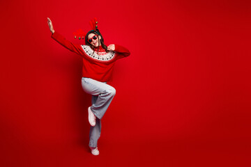 Joyful woman in red christmas sweater dances against a bold red background creating a festive...