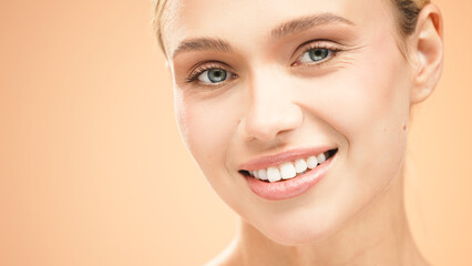 Obraz premium Beautiful young woman with clean fresh skin smiles radiantly against a soft peach background, showcasing natural beauty and confidence in a vibrant portrait