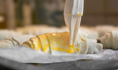Baker brushing egg yolk on raw croissants on baking sheet