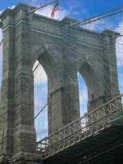 Fototapeta premium Close view of Brooklyn Bridge in New York City showing stone towers, steel cables, and American flag under blue sky
