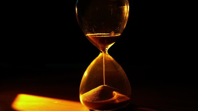 A video frame of an hourglass where golden sand flows, powerfully symbolizing the irreversible passing of time under dramatic, warm light.