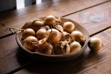 Freshly harvested onions arranged in a rustic bowl on a wooden table in a cozy kitchen setting