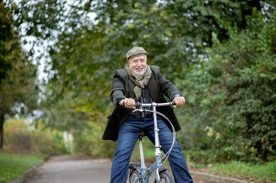 Older man enjoys a joyful bike ride on a peaceful path surrounded by trees in autumn - Powered by Adobe