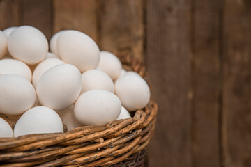 Chicken eggs in large wicker basket with wall of chicken coop, barn or wooden grunge fence in the background. Countryside setting