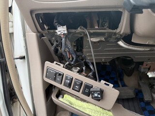Car interior detail showing disassembled dashboard control panel with exposed electrical wiring. Auto repair or diagnostic process in progress, focusing on vehicle electronics and maintenance work.