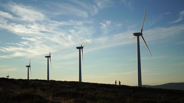 Wind turbines generating renewable energy under blue sky at sunset over hills, Spain