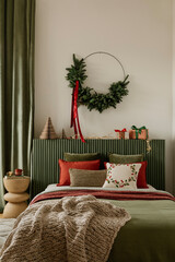 Stylish bedroom decorated for Christmas with green headboard, red pillows, and a simple wreath above the bed.