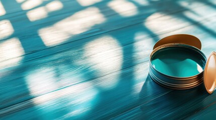 A tin of blue paint sits on a sunlit wooden surface, casting artistic shadows and reflections in a creative workspace.