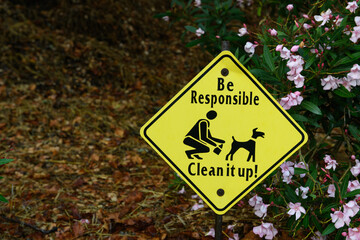 Yellow warning sign on a residential lawn asking dog owners to be responsible and clean up after their pets.