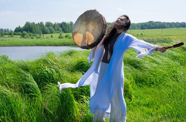 A female shaman in a trance in the white dress drumming in the natural environment