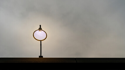 A retro style light lamp on the building rooftop is glowing in warmlight shade, with dark cloudy...