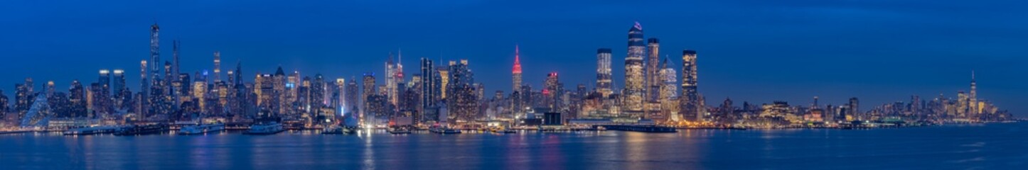 Obraz premium A breathtaking panoramic view of New York City skyline at dusk, showcasing its iconic skyscrapers illuminated against the night sky, reflecting on the water, capturing the vibrant urban atmosphere.
