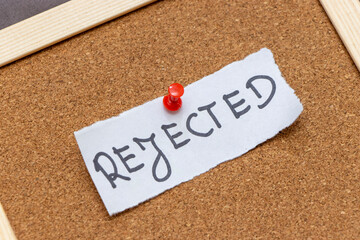 Handwritten word REJECTED pinned to a corkboard with a red pushpin represents rejection or denial in ideas and applications. Ideal for conveying disappointment.