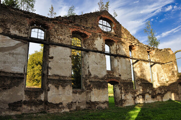 Gostków – ruiny kościoła ewangelickiego z XVIII w. Renesansowy mur z łukowymi oknami w rozświetlonym słońcem wiejskim krajobrazie.